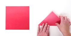 two hands are holding a piece of red paper next to a pink triangle on a white surface