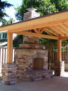 an outdoor fireplace in the middle of a patio with a wooden pergolan roof