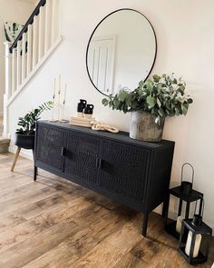 an entryway with a black sideboard, mirror and potted plants on it