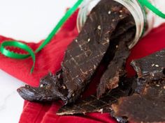 a jar filled with dark chocolate pieces on top of a red cloth next to a green ribbon