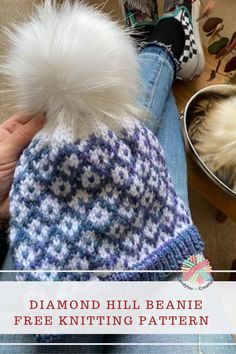 a person holding a white and blue knitted beanie with a pom - pom on it