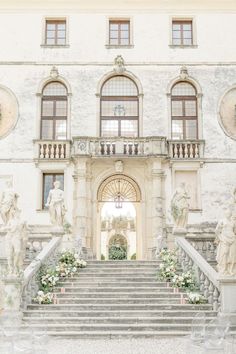 a large white building with many windows and statues on the front steps that lead up to it