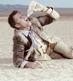 a man laying on the ground drinking from a water bottle in his hand and wearing a tie