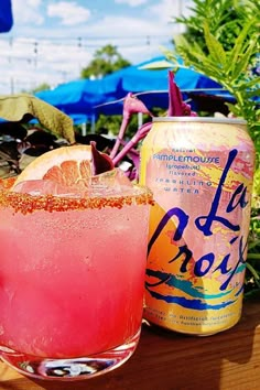 a pink drink sitting on top of a wooden table next to an orange and blue umbrella