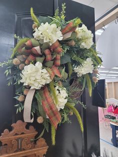 a wreath with white flowers and greenery hanging on a door