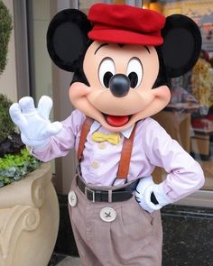 a mickey mouse mascot standing next to a potted plant in front of a building