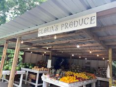 an outdoor produce stand with lots of fruits and vegetables on the tables in front of it