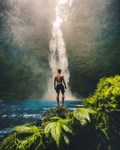 a man standing on top of a rock in front of a waterfall