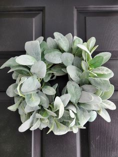 a wreath on the front door with green leaves and greenery hanging from it's side