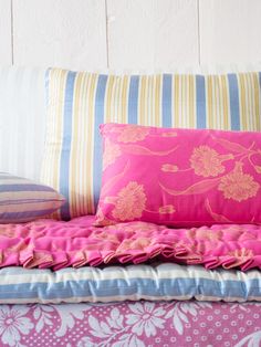 a bed with pink and blue pillows on it's side, next to a striped pillow