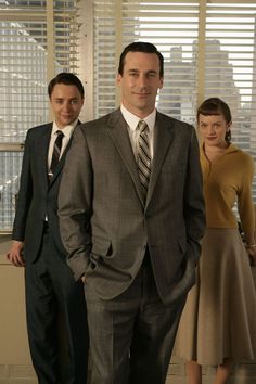 three people in suits and ties standing next to each other with blinds on the window behind them