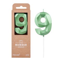 a green cake topper with the number 9 on it in a cardboard box next to a stick