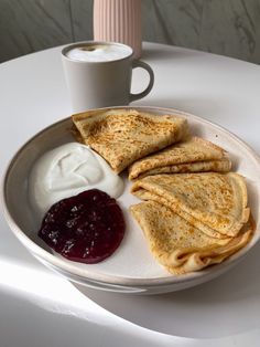 a plate with crepes, yogurt and jam next to a cup