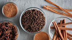 bowls filled with different types of spices on top of a gray cloth next to cinnamon sticks