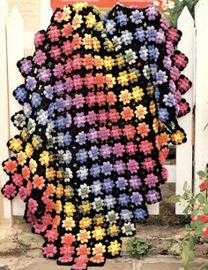 a crocheted blanket sitting on the ground next to a white fence and red door