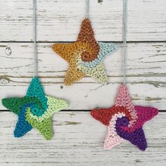 three crocheted stars hanging from strings on a white wooden background, one is multicolored