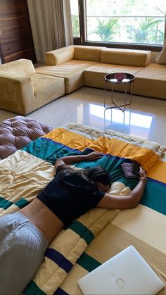 a woman laying on top of a bed in front of a laptop computer next to a window