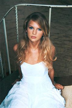 a woman in a white dress sitting on the ground with her hair blowing in the wind