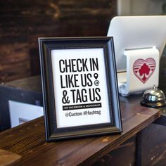 a framed sign sitting on top of a wooden table next to a laptop and mouse