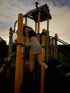 a young woman climbing up the side of a yellow and black playground structure at dusk