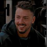 a man with a goatee smiles while sitting in front of a computer monitor screen