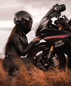 a woman sitting on the ground next to a motorcycle wearing a leather jacket and helmet