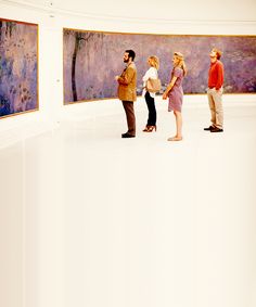 four people are standing in front of two paintings and one is looking up at the sky