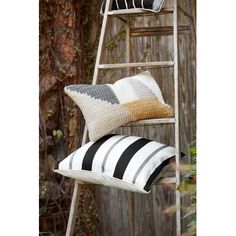 two black and white striped pillows sitting on top of a ladder next to a tree