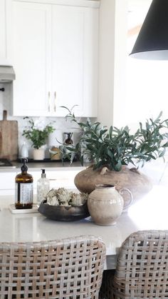 a kitchen with wicker chairs and a table in front of the counter top, surrounded by potted plants