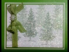 a christmas card with a green ribbon and snow covered pine trees in the back ground