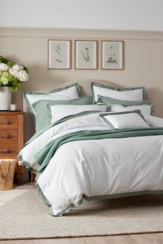 a bed with white and green comforters in a bedroom next to a wooden dresser