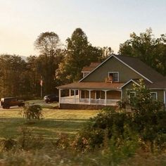 a large house sitting in the middle of a lush green field next to a forest