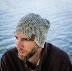 a man with a beard wearing a crocheted hat by the water's edge