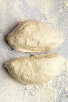 two uncooked pizza doughs on a floured surface