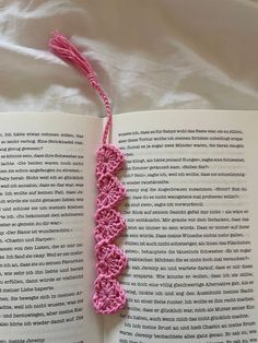 an open book with a pink crocheted string attached to the cover, laying on a bed