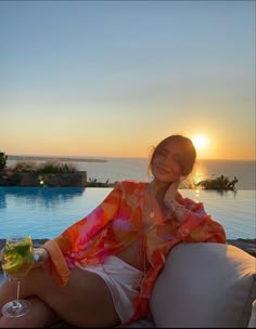 a woman sitting on top of a white couch next to a swimming pool at sunset