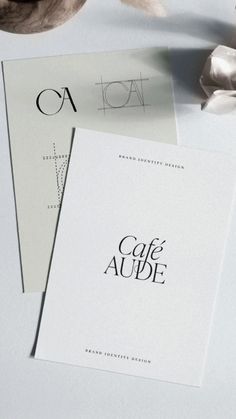 two cards with the words cafe aude on them next to some flowers and feathers