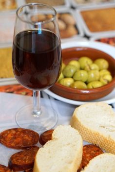 some bread and olives on a table with a glass of red wine in the foreground