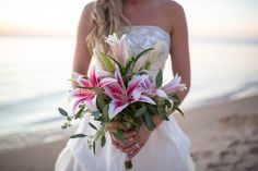 a bride holding a bouquet of flowers on the beach