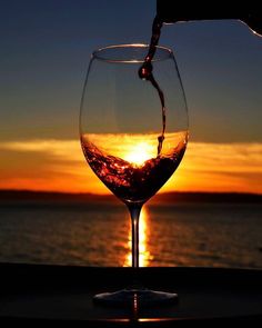 a person pours wine into a glass at sunset over the ocean, with the sun setting in the distance