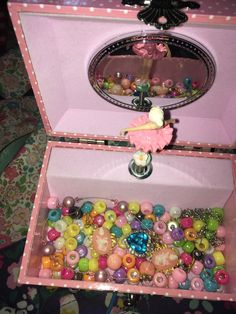 an open pink box filled with lots of colorful beads and buttons on top of a table