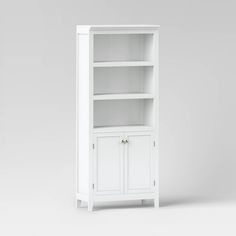 a white bookcase with two doors and one door open on the bottom shelf, in front of a gray background