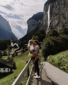 a man and woman standing next to each other in front of a mountain with a waterfall