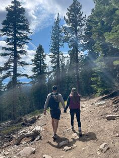 two people walking down a trail in the woods on a sunny day with trees and rocks