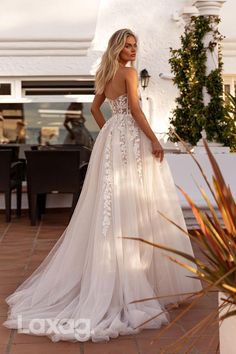 a woman in a white wedding dress standing on a brick patio with her back to the camera