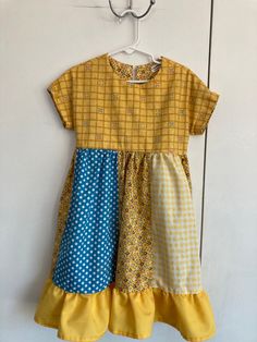 a yellow and blue dress hanging on a wall with a hanger in front of it