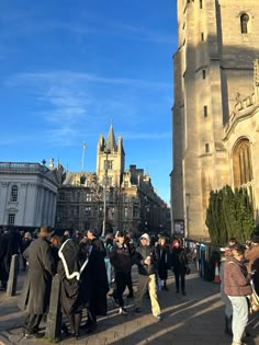 many people are walking around in front of an old building with tall towers and spires