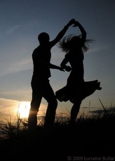 two people are dancing in the grass at sunset