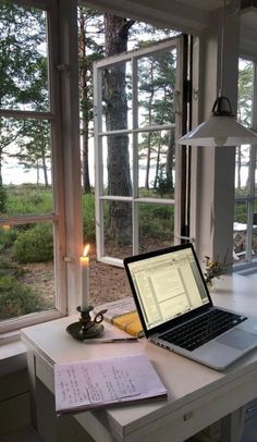 an open laptop computer sitting on top of a desk next to a candle and window