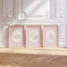 three pink and white framed pictures sitting on top of a wooden floor next to a wall